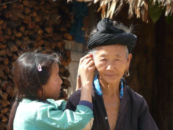 A young girl carefully cleaning the ear lobe of her grandma outside their home in the Laos