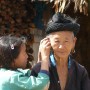 A young girl carefully cleaning the ear lobe of her grandma outside their home in the Laos